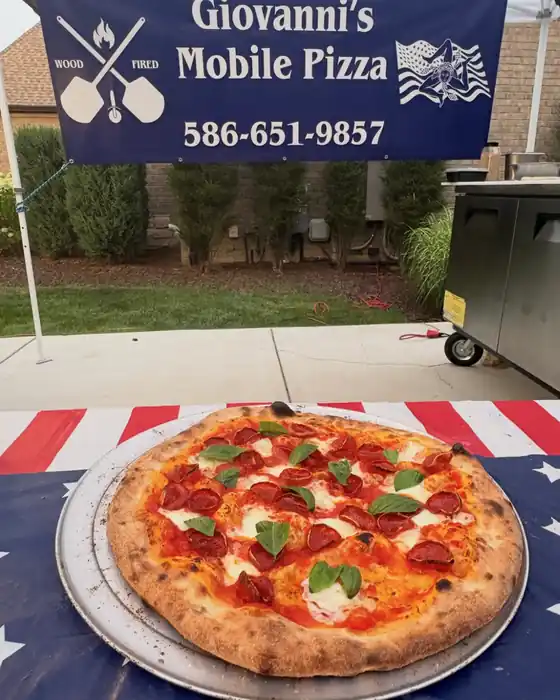 A real Giovanni's wood-fired pepperoni and basil pizza in front of the Giovanni's Mobile Pizza banner