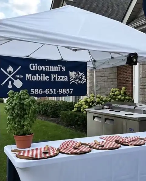 Giovanni's Mobile Pizza tent setup with banner, fresh basil, and red-checkered pizza peels
